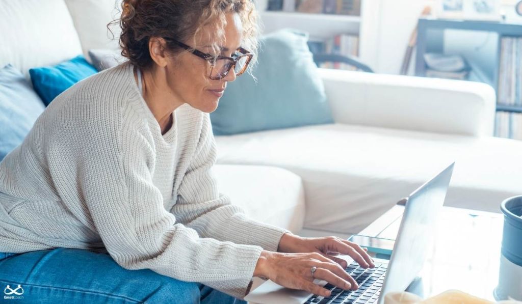 une femme dans son salon en train de prendre un accompagnement en coaching de développement personnel en visio sur son ordinateur avec Emoticoach genève