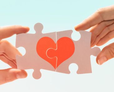 Deux mains tiennent une pièce de puzzle qui forme un coeur quand on les associent pour marque l'importance des liens humains